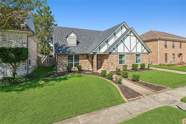 tudor-style house with a front lawn, roof with shingles, fence, and brick siding