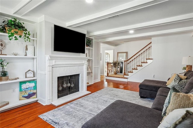 living room featuring a brick fireplace, beam ceiling, stairway, and wood finished floors