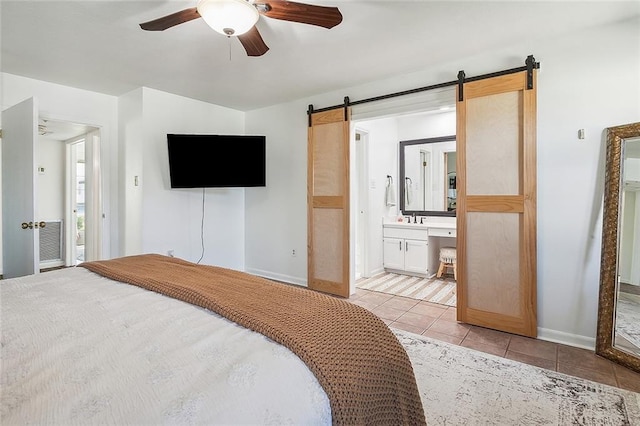 bedroom featuring ensuite bathroom, a barn door, light tile patterned flooring, a sink, and baseboards