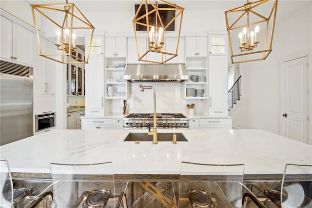 kitchen with wall chimney range hood, hanging light fixtures, white cabinetry, a kitchen bar, and stainless steel appliances