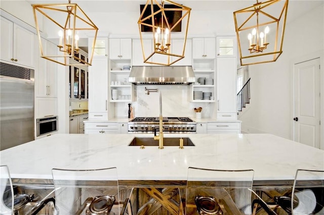 kitchen with open shelves, range hood, a notable chandelier, stainless steel appliances, and a sink