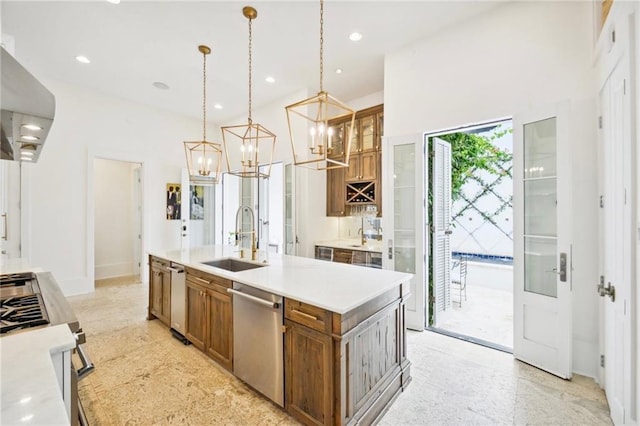 kitchen with an island with sink, extractor fan, stainless steel appliances, sink, and decorative light fixtures