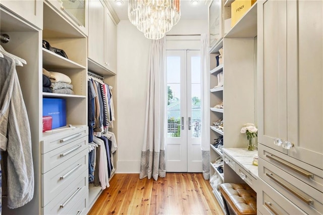 walk in closet with french doors, a notable chandelier, and light wood-type flooring