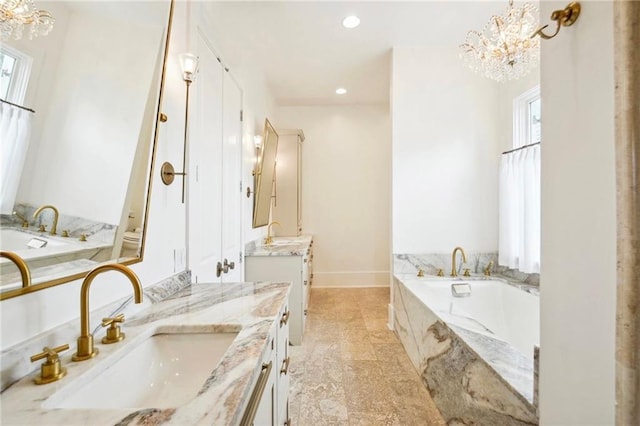 full bathroom with two vanities, a notable chandelier, a bath, and a sink