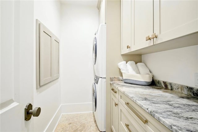 clothes washing area with baseboards, cabinet space, and stacked washer and clothes dryer