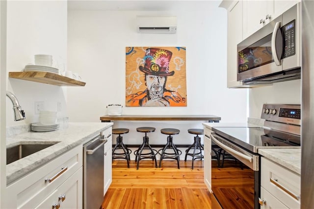 kitchen with a wall unit AC, light stone counters, white cabinetry, light hardwood / wood-style flooring, and stainless steel appliances