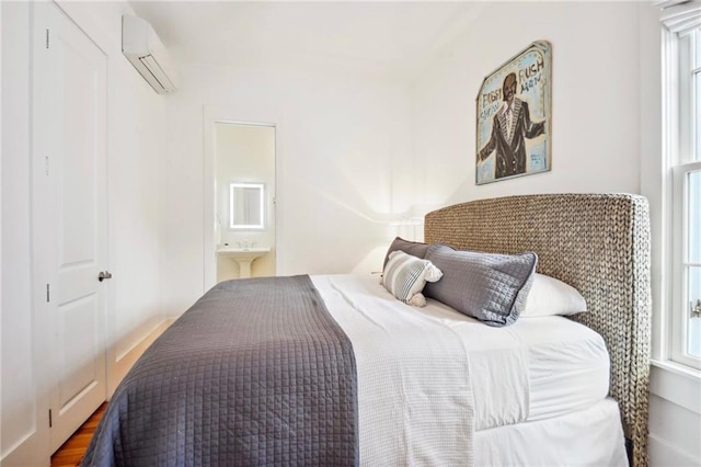 bedroom with ensuite bath, multiple windows, a wall mounted air conditioner, and wood finished floors