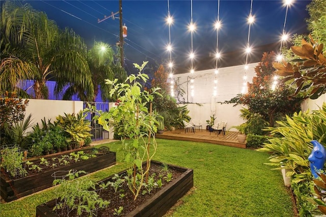 yard at twilight with a wooden deck, a vegetable garden, and fence