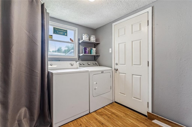 laundry area with light hardwood / wood-style floors, a textured ceiling, and washer and clothes dryer