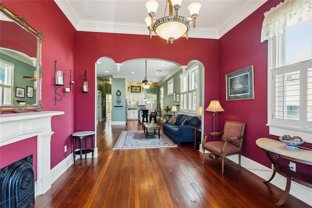 sitting room with ornamental molding, a wealth of natural light, ceiling fan with notable chandelier, and dark hardwood / wood-style flooring