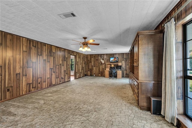 unfurnished living room featuring ceiling fan, wooden walls, and light carpet