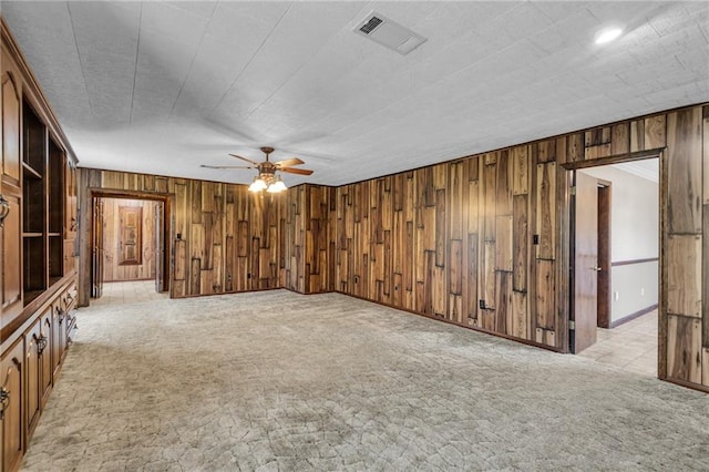 spare room with ceiling fan, light colored carpet, and wooden walls