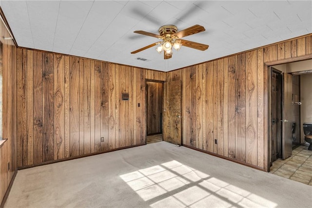 unfurnished bedroom featuring light carpet, connected bathroom, wooden walls, and ceiling fan