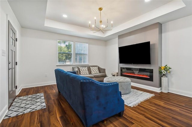 living room with an inviting chandelier, a raised ceiling, and dark hardwood / wood-style floors