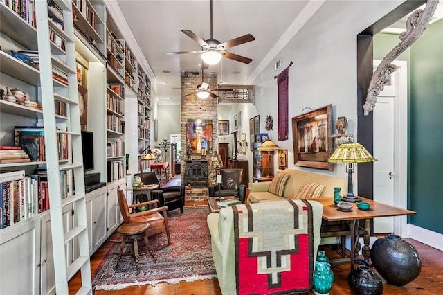 sitting room featuring crown molding, a wood stove, ceiling fan, wood finished floors, and baseboards