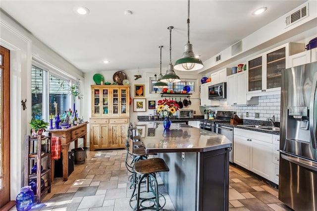 kitchen with a sink, visible vents, appliances with stainless steel finishes, a kitchen bar, and glass insert cabinets