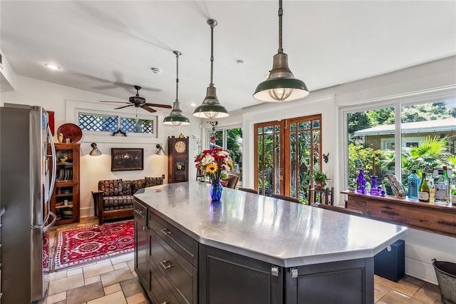 kitchen featuring stone tile floors, stainless steel countertops, freestanding refrigerator, a kitchen island, and dark cabinetry