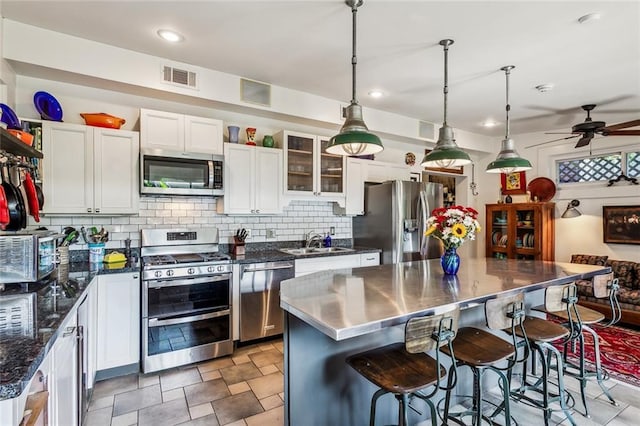 kitchen featuring stainless steel appliances, stainless steel countertops, white cabinetry, visible vents, and decorative backsplash