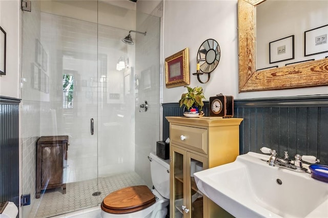 full bathroom with a stall shower, wainscoting, a sink, and toilet