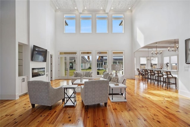 living area with baseboards, light wood-style floors, a glass covered fireplace, beamed ceiling, and a chandelier