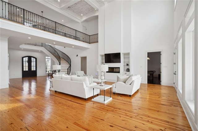 living area with light wood-type flooring, beam ceiling, a glass covered fireplace, french doors, and stairs