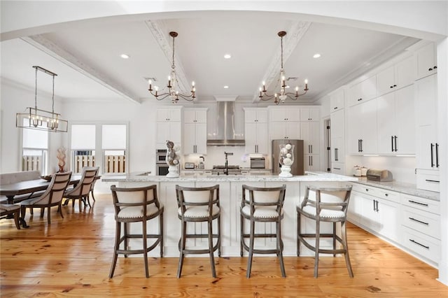 kitchen featuring light wood-style flooring, white cabinets, crown molding, wall chimney exhaust hood, and a notable chandelier