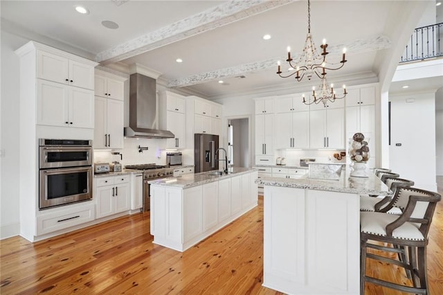 kitchen with wall chimney range hood, ornamental molding, light wood-style flooring, appliances with stainless steel finishes, and white cabinetry