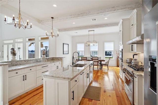 kitchen with a center island with sink, a sink, under cabinet range hood, stainless steel appliances, and an inviting chandelier