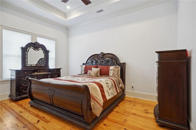 bedroom featuring visible vents, baseboards, a tray ceiling, ornamental molding, and light wood-style flooring