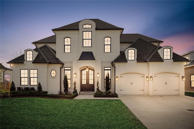 french country style house featuring stucco siding, french doors, concrete driveway, an attached garage, and a front yard