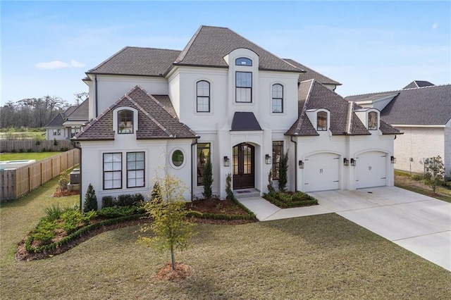 french country home with stucco siding, a front lawn, fence, concrete driveway, and a shingled roof