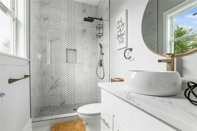 bathroom with a tile shower, toilet, and vanity