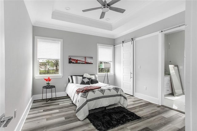 bedroom with a barn door, ceiling fan, crown molding, light hardwood / wood-style flooring, and a raised ceiling