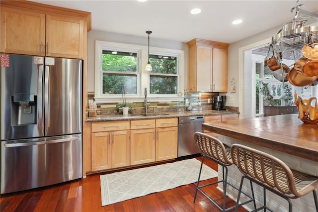 kitchen featuring dark hardwood / wood-style floors, stainless steel appliances, sink, dark stone counters, and hanging light fixtures