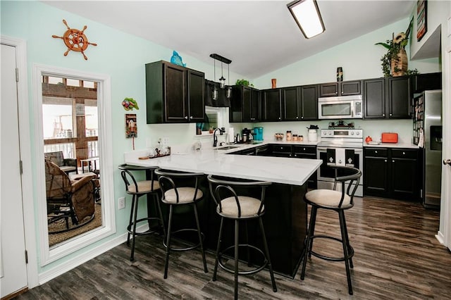 kitchen with appliances with stainless steel finishes, dark hardwood / wood-style flooring, kitchen peninsula, vaulted ceiling, and pendant lighting