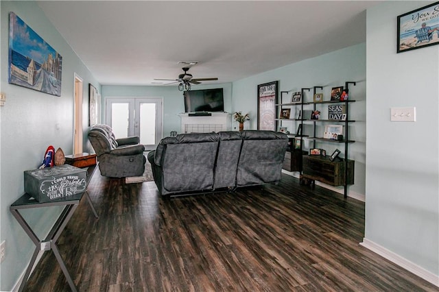 living room with french doors, ceiling fan, a tiled fireplace, and dark hardwood / wood-style flooring