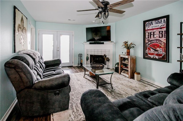 living room featuring french doors, hardwood / wood-style floors, a tiled fireplace, and ceiling fan