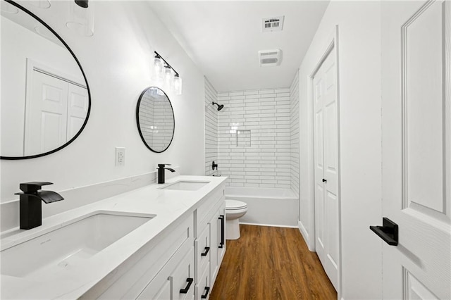 full bathroom with tiled shower / bath combo, vanity, hardwood / wood-style floors, and toilet