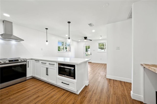 kitchen featuring wall chimney exhaust hood, white cabinetry, decorative light fixtures, stainless steel appliances, and hardwood / wood-style floors