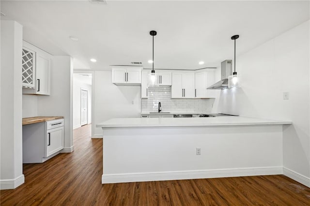 kitchen featuring dark hardwood / wood-style flooring, kitchen peninsula, wall chimney range hood, white cabinetry, and decorative light fixtures