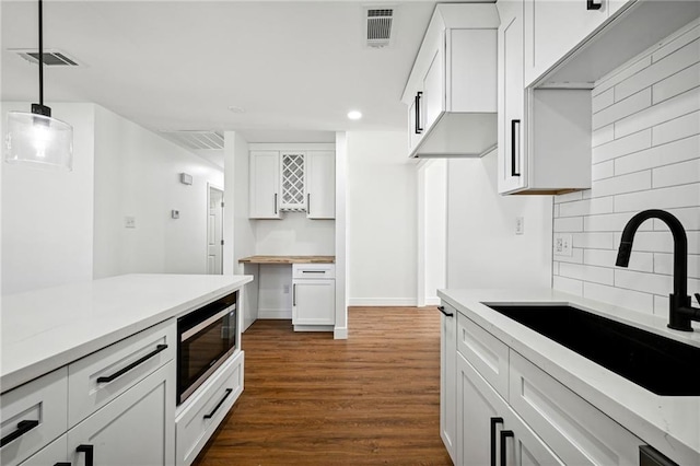 kitchen with dark hardwood / wood-style floors, stainless steel microwave, white cabinetry, sink, and hanging light fixtures