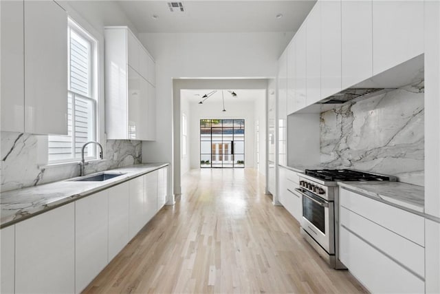 kitchen featuring stainless steel stove, white cabinets, sink, and a healthy amount of sunlight