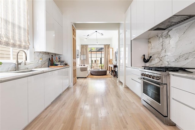 kitchen featuring light wood-type flooring, stainless steel stove, sink, backsplash, and white cabinetry