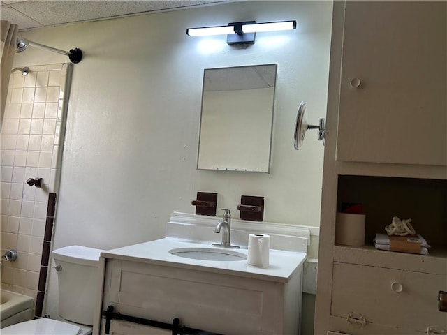 full bathroom featuring a drop ceiling, vanity, tiled shower / bath combo, and toilet