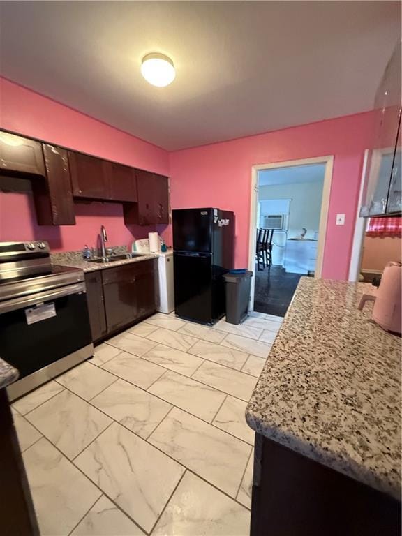 kitchen featuring stainless steel electric range, black fridge, sink, light stone counters, and dark brown cabinetry