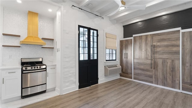 kitchen featuring light wood-type flooring, stainless steel range, beam ceiling, an AC wall unit, and white cabinetry