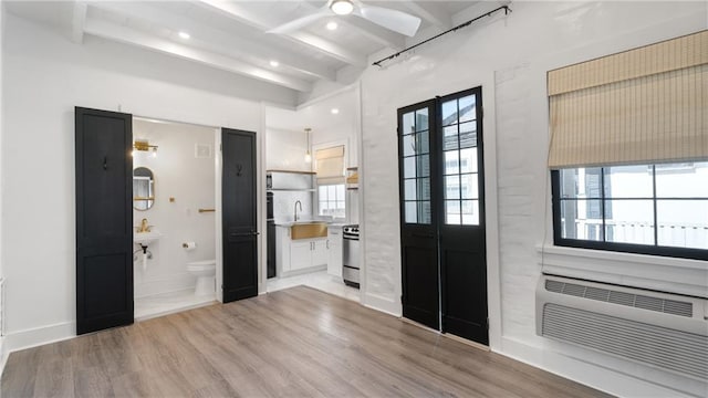 foyer entrance with beamed ceiling, a wall mounted air conditioner, sink, and light hardwood / wood-style floors