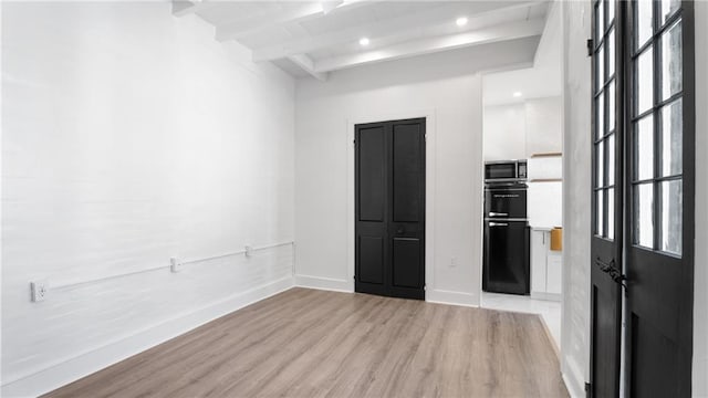 empty room with beam ceiling and light hardwood / wood-style flooring