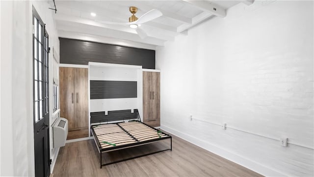 bedroom with ceiling fan, hardwood / wood-style flooring, beam ceiling, and an AC wall unit