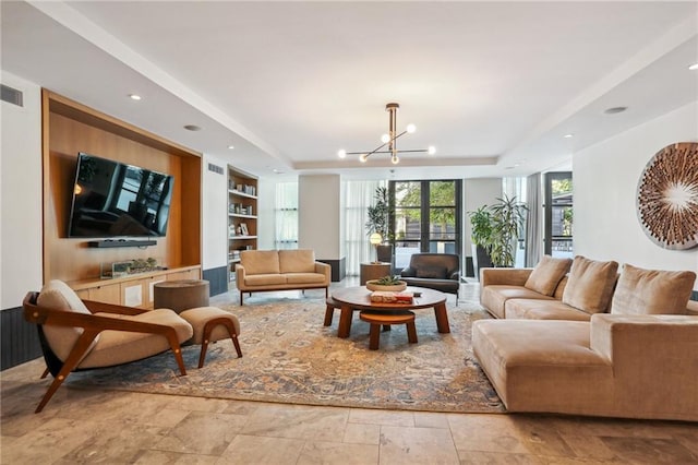 living room with a notable chandelier, built in shelves, and a raised ceiling